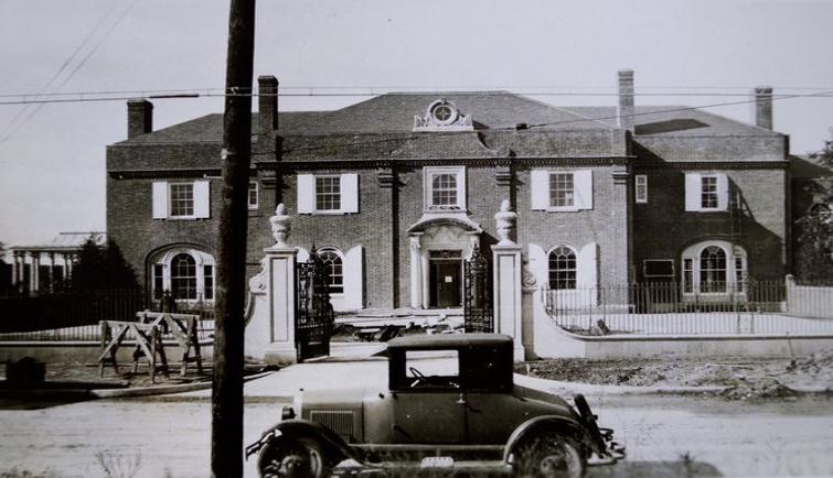布鲁克比的黑白老照片前面停着一辆早期的汽车. 两层楼，有窗户，前面有一扇大门.