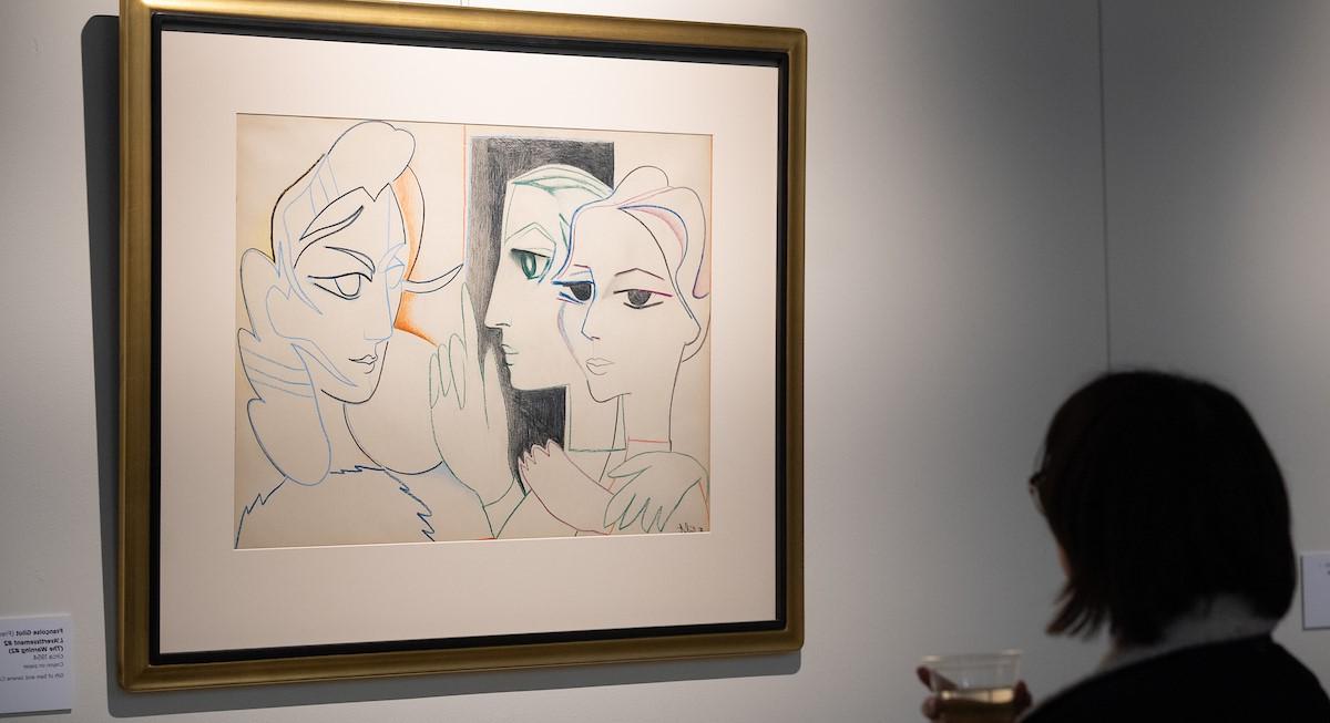 一幅有框的吉洛画，名为“警告#2”，画的是两个女人, 一个用手指指着另一个. 一位观众站在前景.
