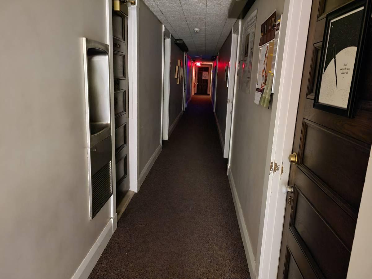 晚上三楼走廊的照片. 狭窄而布满了门. 在尽头有一个发光的红色出口标志.